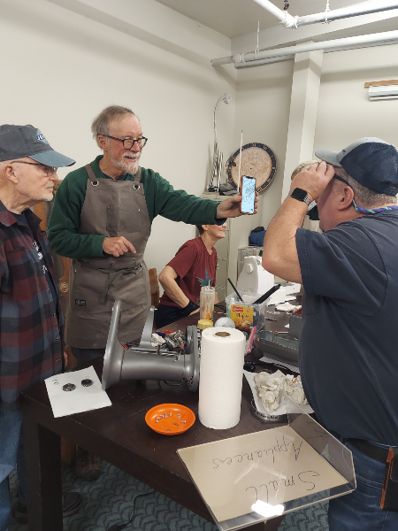John Beaston (holding phone), Dick Park (left) and Gary Bond are among the expert fixers at the monthly Repair Cafe. They often work together to fix what they can for resale. Photo courtesy: Heart of Cartm