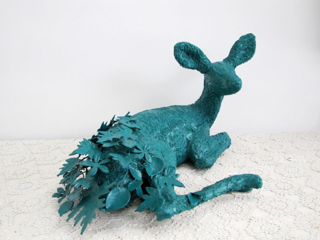 green sculpture of a your deer (potentially kangaroo) in a reclining position -posterior made of plants, leaves, petals